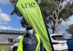 Alan Gray stands out the front of a une banner wearing SportUNE dark blue jumper and a mask
