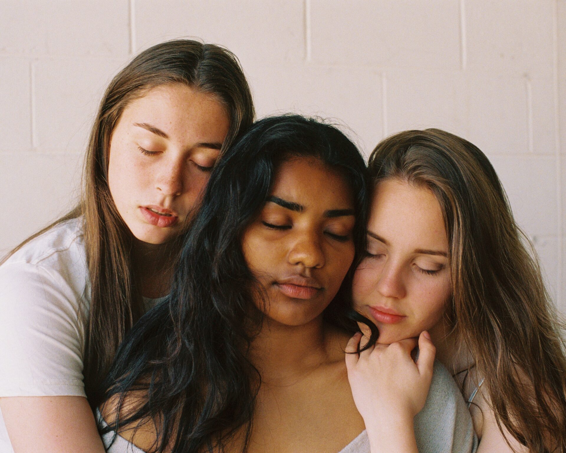 three girls hold eachother in a group hug with their eyes closed, they seem content.