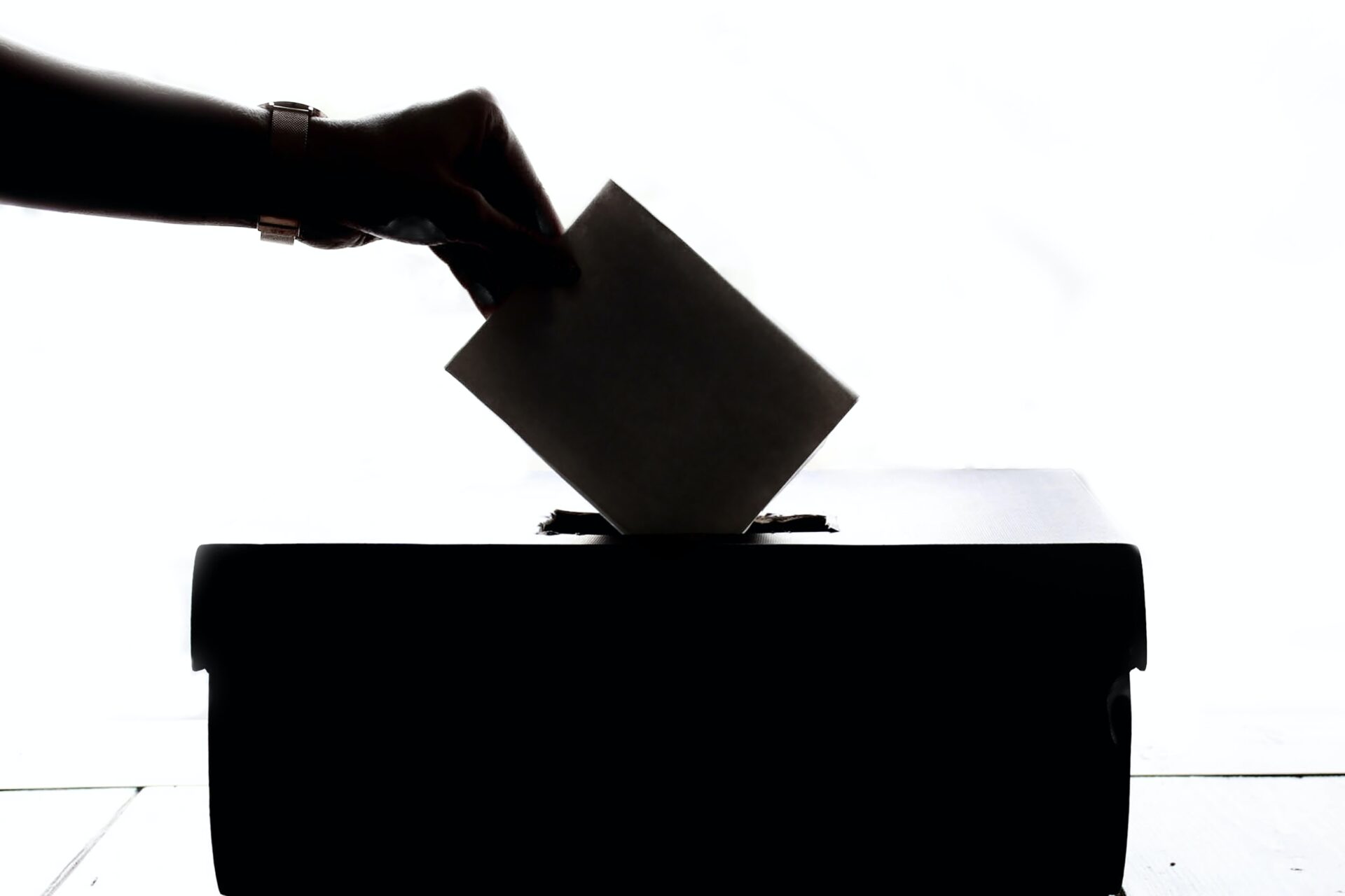 black and white images of a hand putting an envelope into a voting box