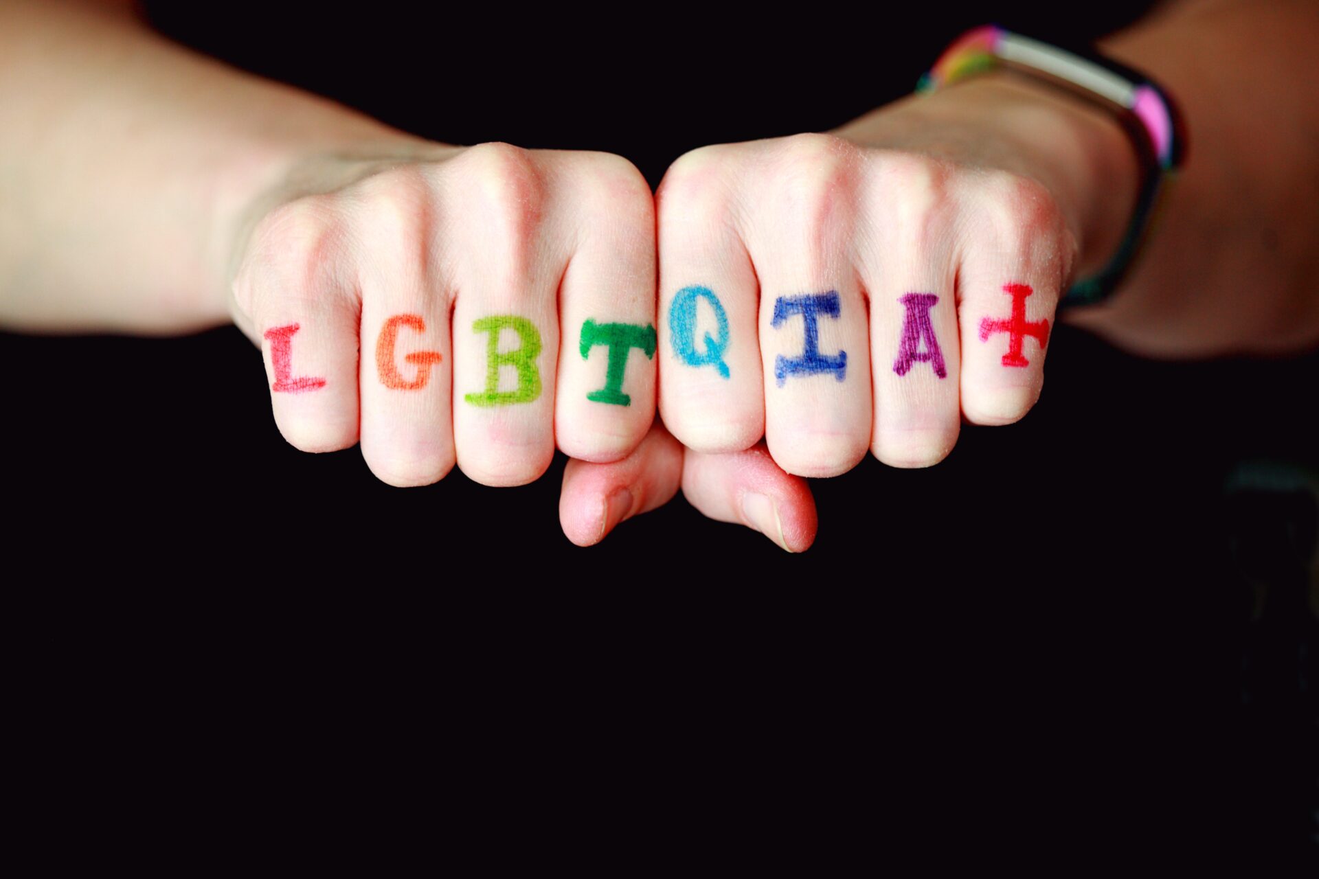 two hands forming fists with the letters LGBTQIA on each finger