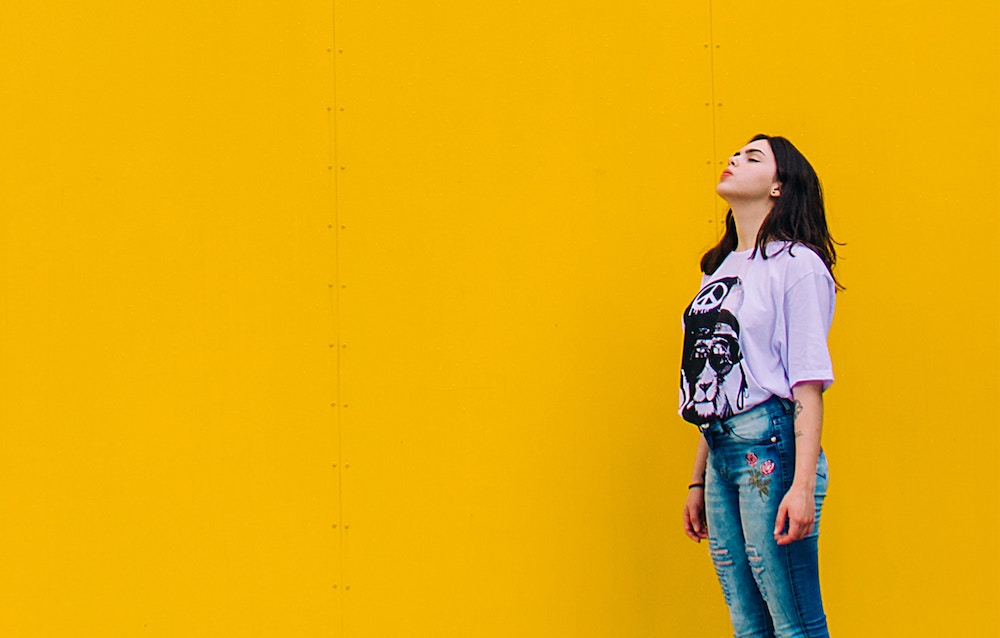 girl standing in front of a yellow wall looking to the sky