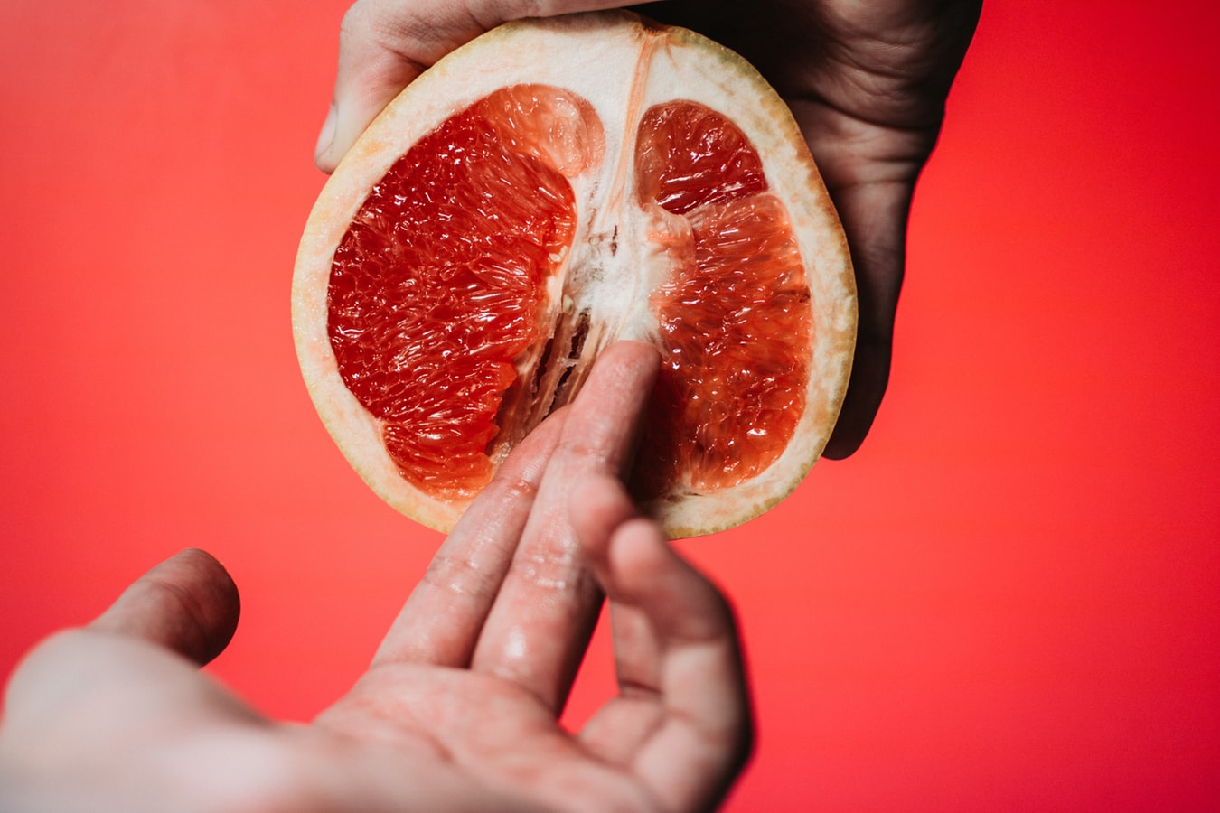 One hand holding half of a grapefruit, while another hand touches the grapefruit.