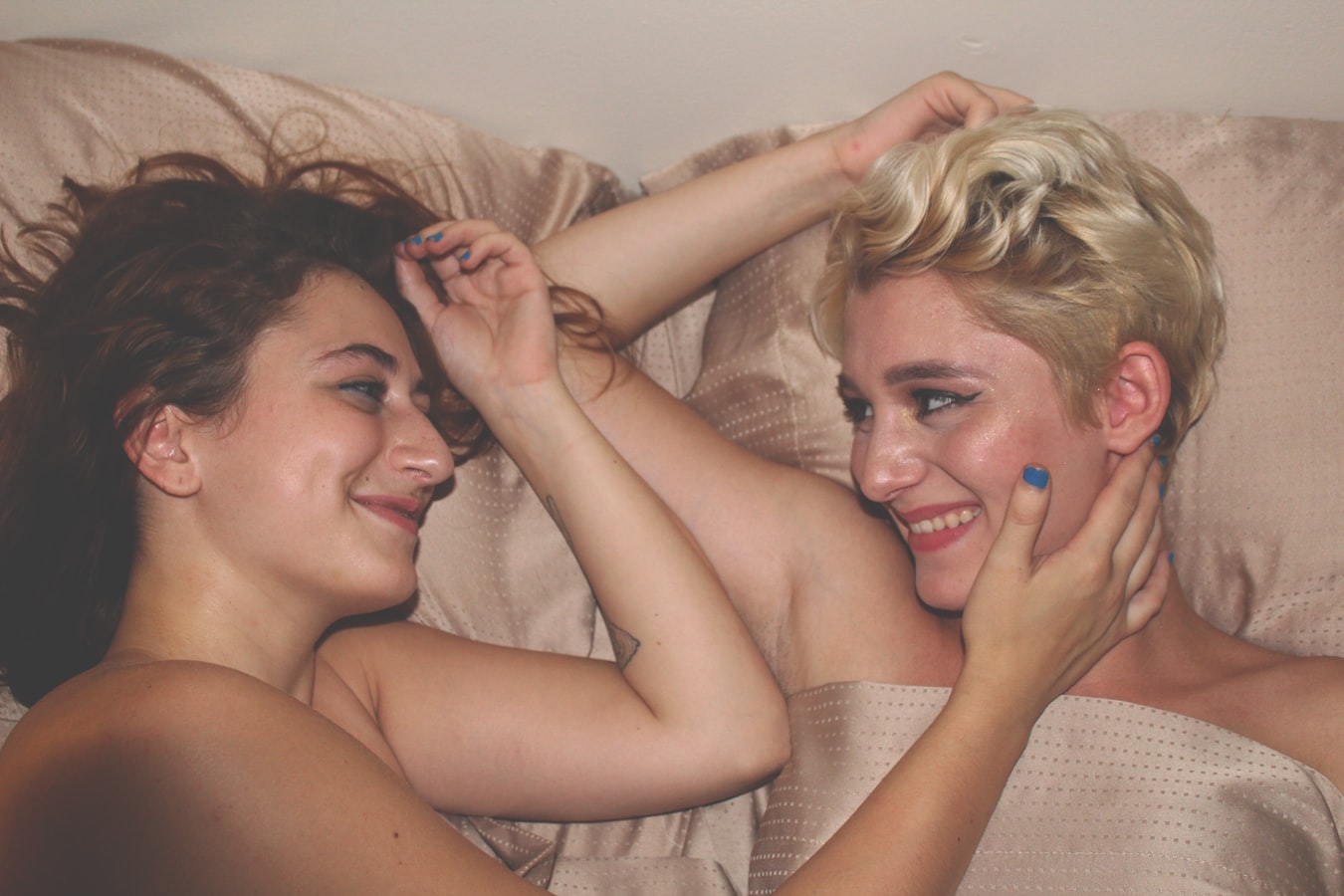 two people, smiling at each other, laying in a bed with beige sheets