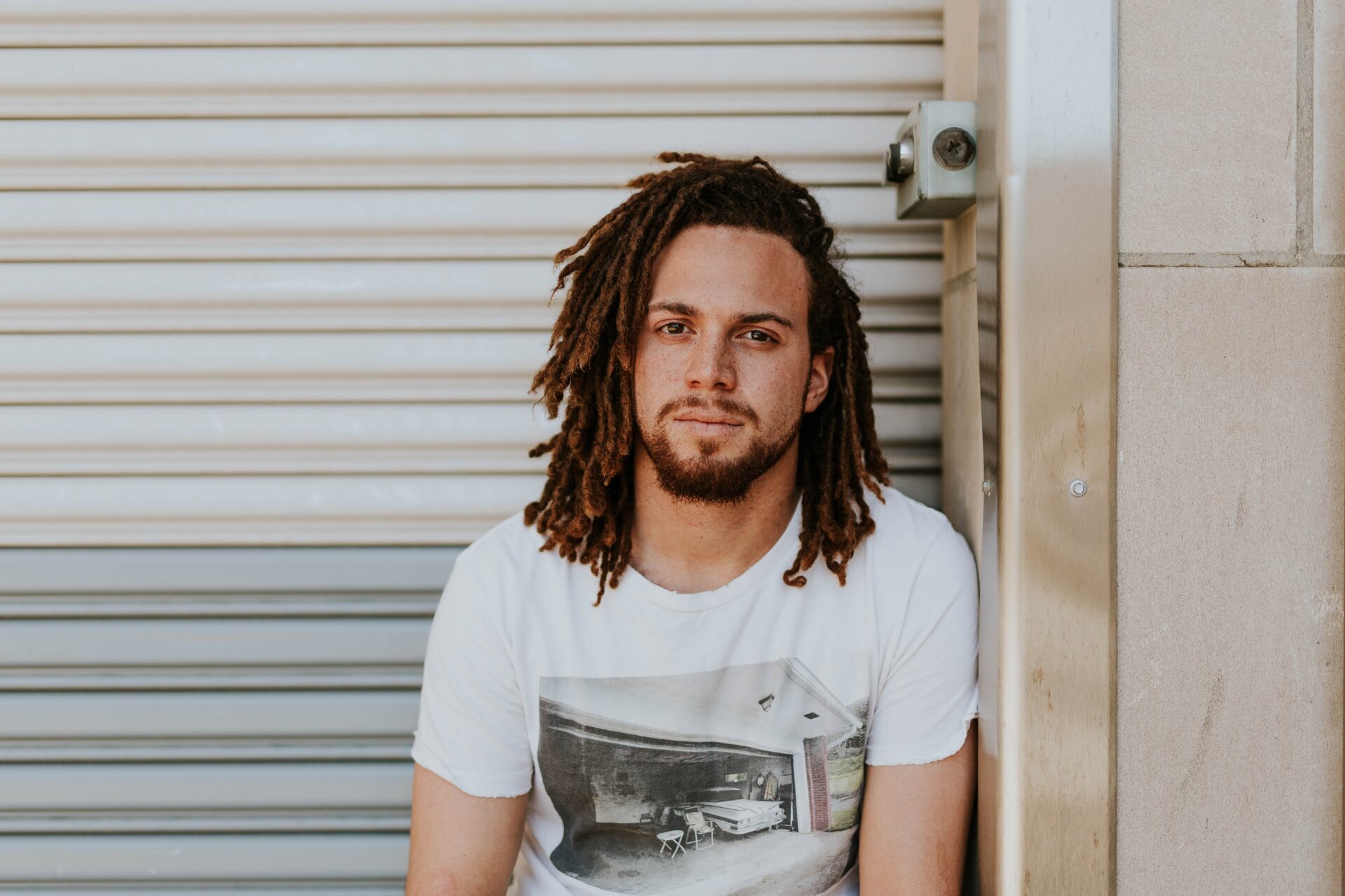 young man with dreadlocks sitting in front of a roller door