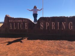 Laura Murray stands on a long rock wall with the words Alice Springs on the front