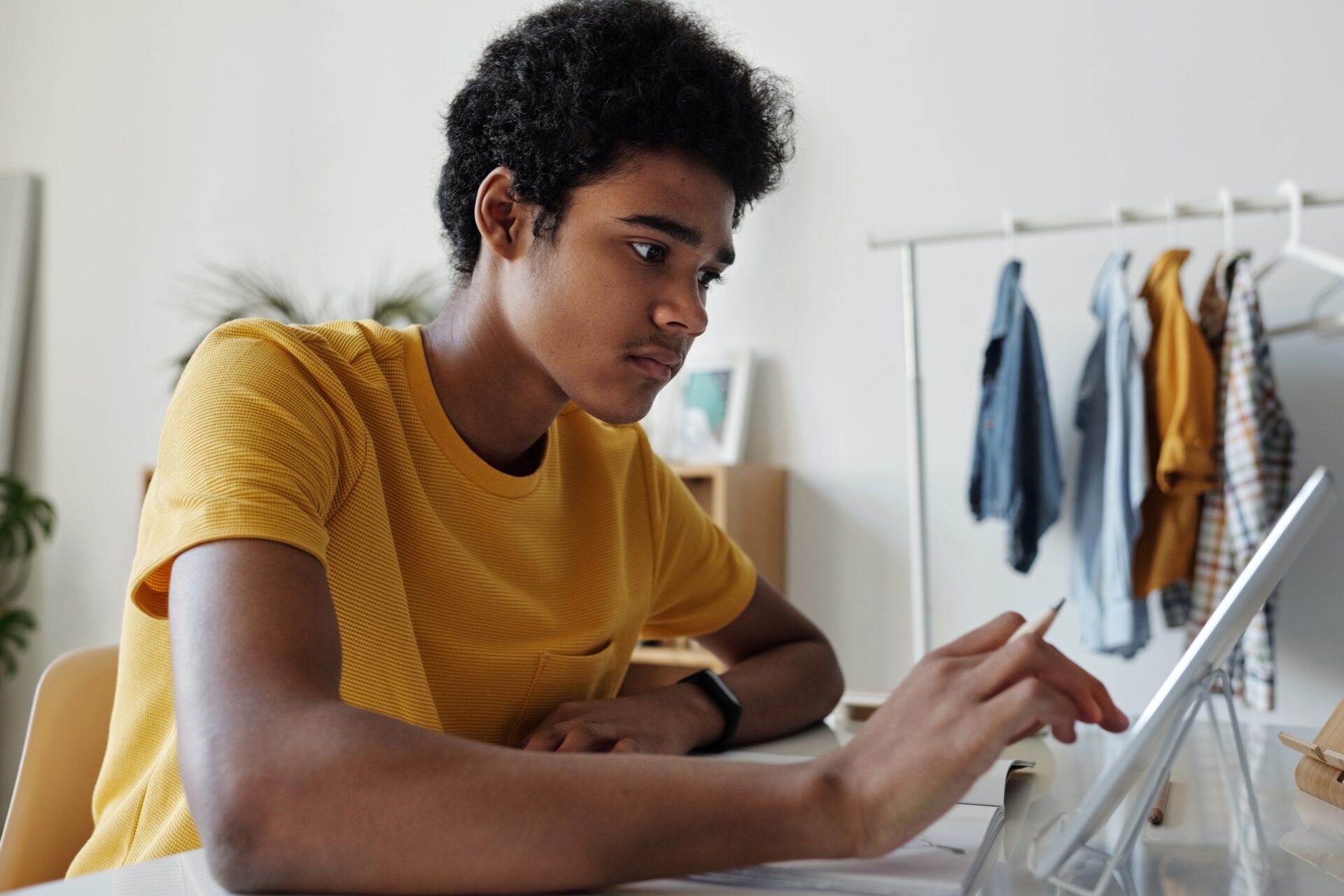 boy in yellow shirt sits at desk looking at his tablet