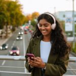 Brunette,Indian,Woman,In,Headphones,Using,Mobile,Phone,While,Walking 
